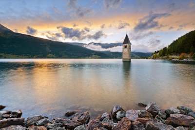 Unter dem Reschensee in Italien befindetet sich ein überschwemmtes Dorf und nur der Kirchturm schaut aus dem Wasser heraus.