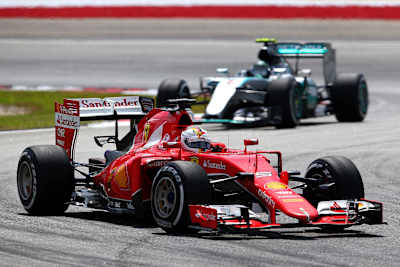 Sebastian Vettel of Germany and Ferrari passes Nico Rosberg in the opening phase of the Malaysia Formula One Grand Prix at Sepang Circuit.