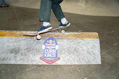 Nahaufnahme eines Feeble Grinds an einem hohen Curb. Der Skater ist oberhalb der Knie abgeschnitten. Das Curb hat unzählige Skatespuren.