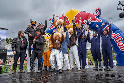 Teams in vibrant costumes celebrate their victory on the Red Bull Olabil 2025 podium in Trondheim, Norway, against the iconic Red Bull backdrop and festive event atmosphere