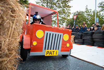 A creative soapbox racer speeds through hay bales at Red Bull Olabil in Trondheim, Norway, as enthusiastic crowds cheer on the daring 2025 event