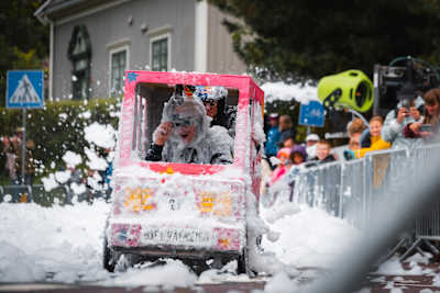 A contestant in a soapbox car races through clouds of foam during Red Bull Olabil 2025, captivating crowds in Trondheim, Norway with kinetic, high-octane creativity and excitement