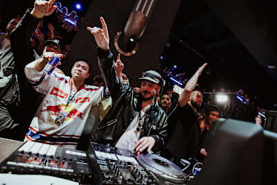 DJ Justakid tritt beim Red Bull BC One Germany 2025 in der Alten Münze in Berlin auf, umgeben von jubelnden Fans und DJ-Equipment