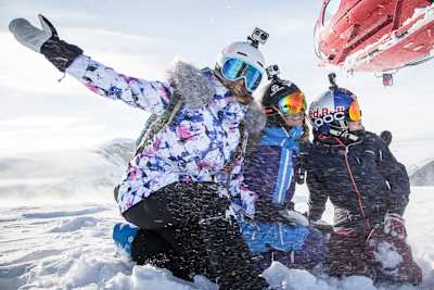A still image from the movie Shades of Winter: BETWEEN featuring three female freeskiers in the snow beside a helicopter.
