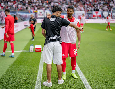 RB Leipzig-Spieler Benjamin Henrichs und eSportler Umut Gültekin begrüßen sich.