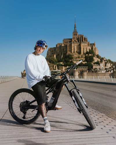 Kriss Kyle pose avec son VTT devant le Mont-Saint-Michel lors du tournage de son projet vidéo.