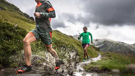 Two people trail running on a wet day over a muddy hillside.