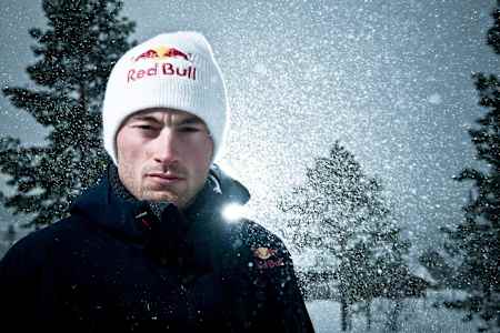 Petter Northug schaut ernst in die Kamera, trägt ein Red Bull Beanie-und Ski-Jacke und ist im Hintergrund von einem schneebedeckten Wald umgeben.