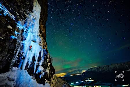 Climbing a frozen waterfall in Lyngen, Norway with the Aurora Borealis in the sky.