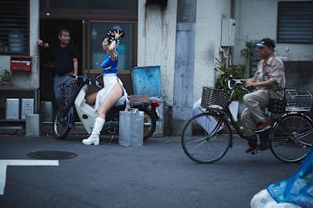 出発前に、お店の主人と談笑。すらりと伸びた美脚の隣で、無骨な岡持ちが存在感を放つ。