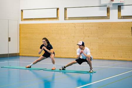 Mathilde Gremaud und Fabian Bösch machen Side Lunges in der Turnhalle.