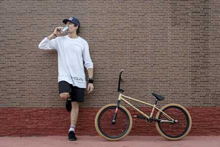 BMX flatlander Viki Gomez sips Red Bull while standing beside his bike.