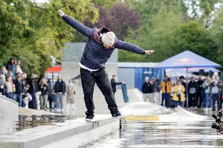 Tory Pudwill in Winterjacke macht einen langen Backside Tailslide an einer Ledge im verregneten North Brigade Skatepark