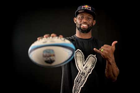 South African professional rugby star Siya Kolisi holding rugby ball out to camera.