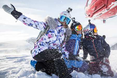 A still image from the movie Shades of Winter: BETWEEN featuring three female freeskiers in the snow beside a helicopter.