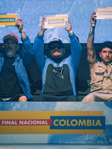 En 2026, tres artistas levantan carteles de Marithea en el escenario de la Final Nacional de Red Bull de Colombia, en Bogotá, con latas de Red Bull como telón de fondo de la celebración