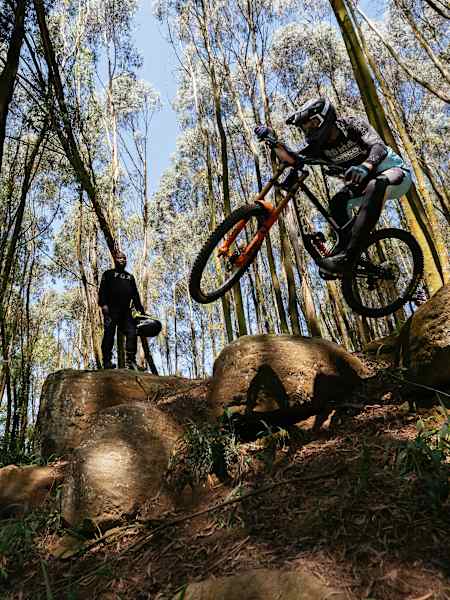 Greg Minnaar launches his mountain bike over rocky terrain as Eugene Khoza watches during filming of What We Know Episode 2 in Pietermaritzburg, South Africa, on 9 December 2025