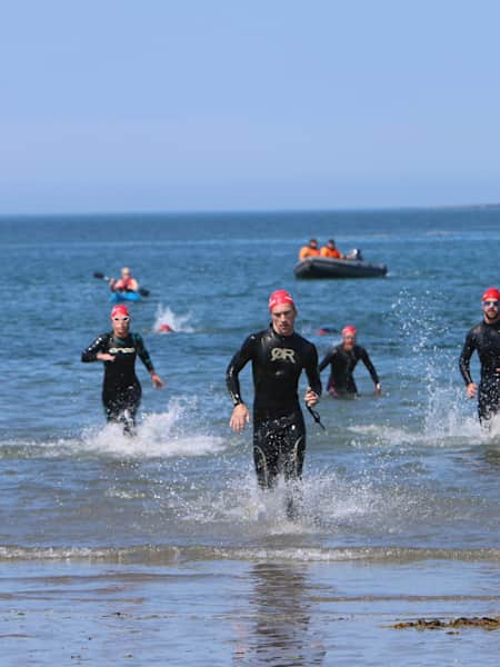 swimmers coming out of the water in wetsuits after long swim