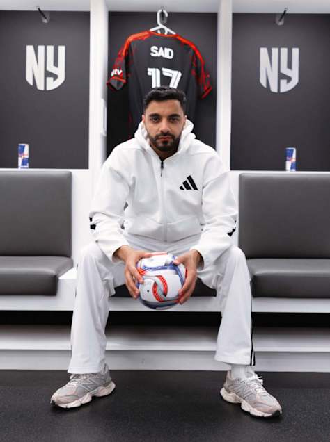 Saïd Dorbani, alias Pieds Carrés, pose dans le vestiaire des New York Red Bulls, avec un ballon entre les mains et son maillot derrière lui.