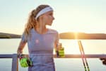 Female Red Bull athlete standing by the railing in front of a lake with a Red Bull can after achieving her running goals