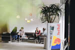 Red Bull employees sitting on couches in the Red Bull HQ in Elsbethen, talking to each other and working together with a Red Bull refrigerator in the front 