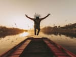 Red Bull athlete Neguin jumps up in the air on a pier by a lake at sunset while spreading his arms